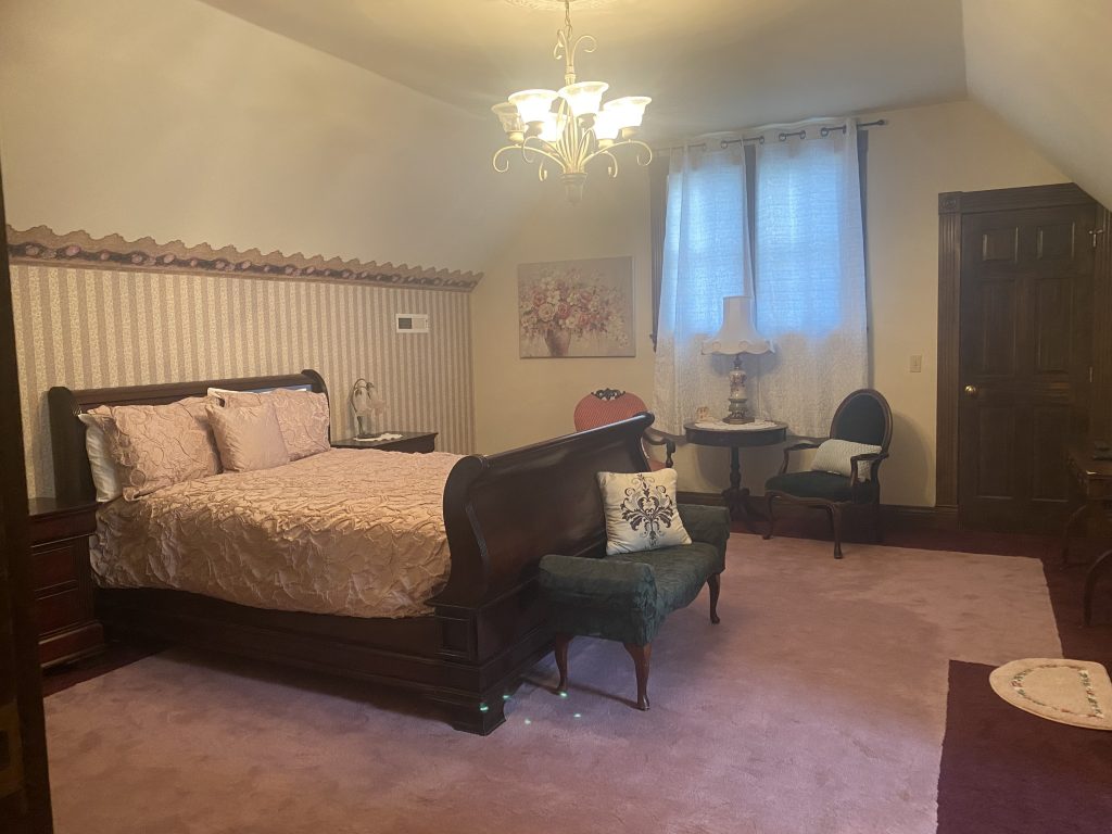 Rose room. Shows a sleight bed, striped wall paper, 2 chairs, table and lamp.